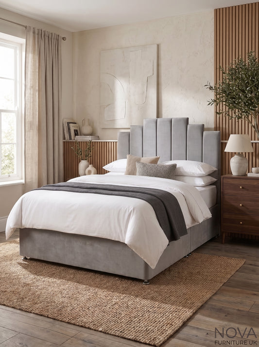 A modern upholstered bed in a styled bedroom setting. The bed features a tall, channel-tufted headboard and a matching upholstered base in a light gray fabric, dressed with white bedding, a dark gray throw blanket, and neutral pillows.