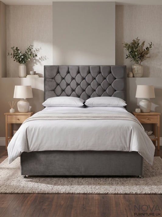 A gray upholstered bed frame with a tufted diamond-pattern headboard and matching footboard, dressed in white bedding, set in a styled bedroom with wooden nightstands, lamps, and a textured rug.